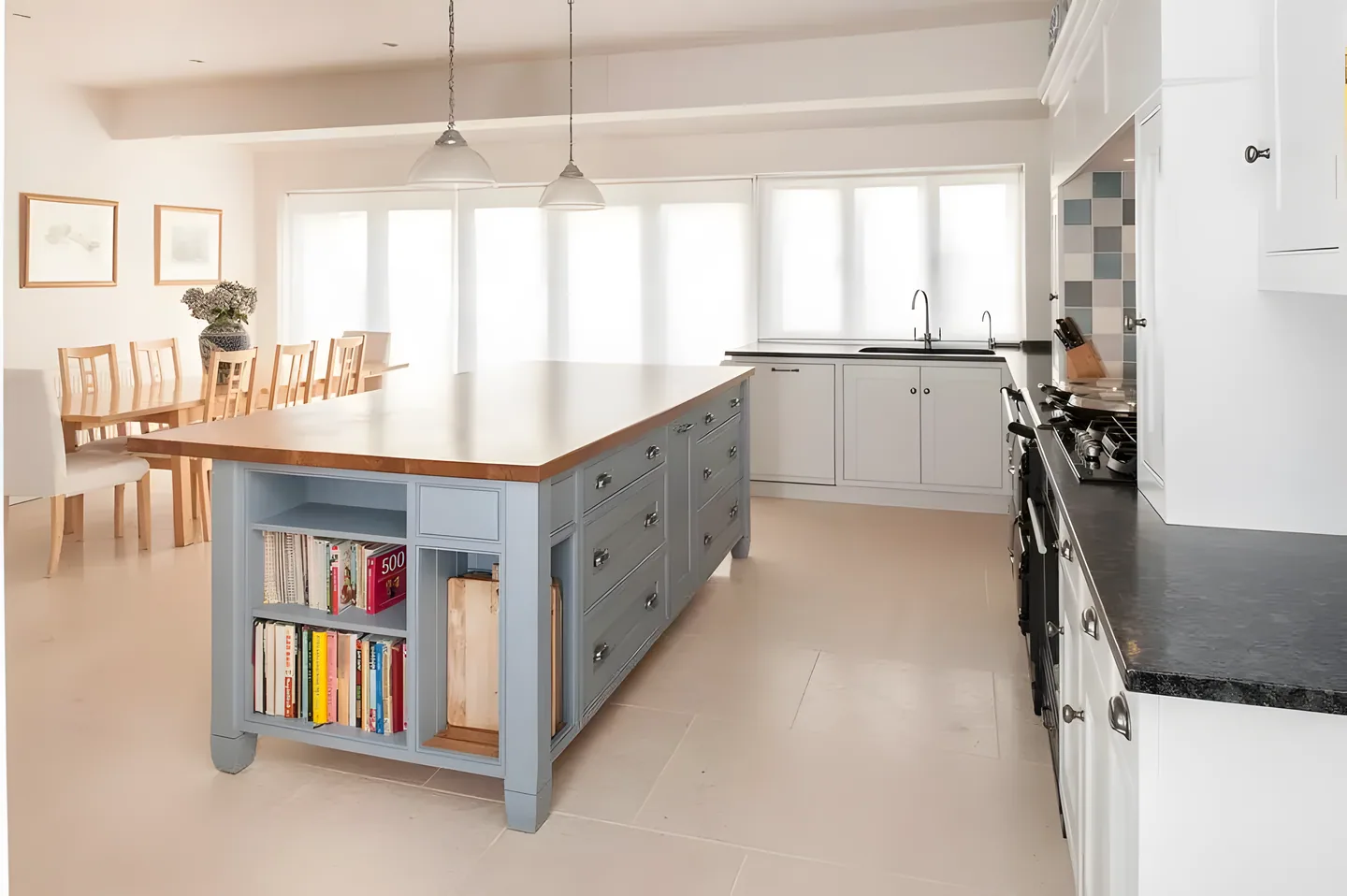 A grey painted island with an oak worktop and open bookshelves