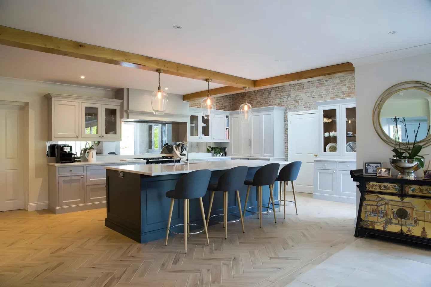 A navy painted kitchen island with bar stools beneath an oak beam, with painted cabinetry and oak doors behind