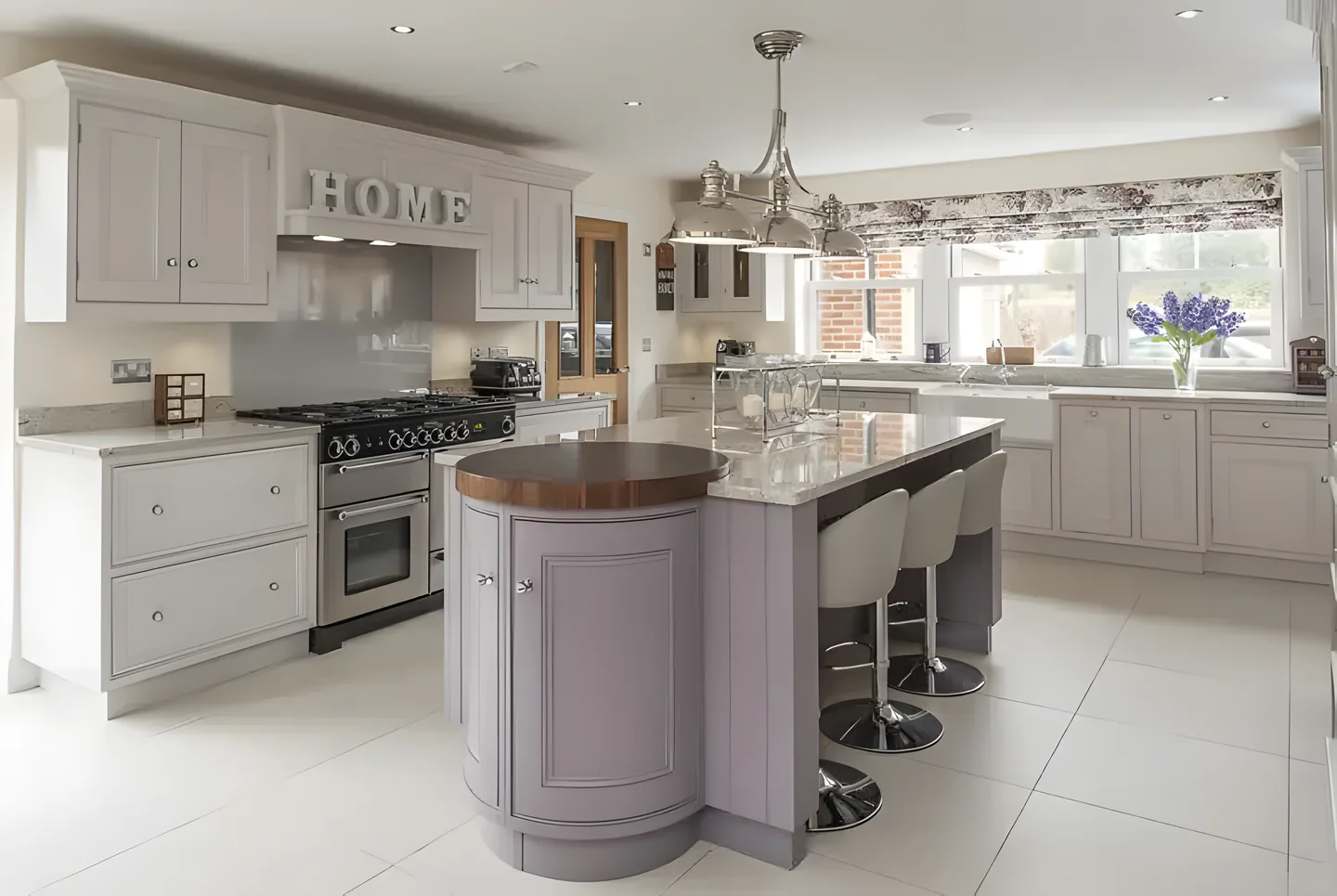 A soft mauve-grey curved island with an oak top in a bright kitchen