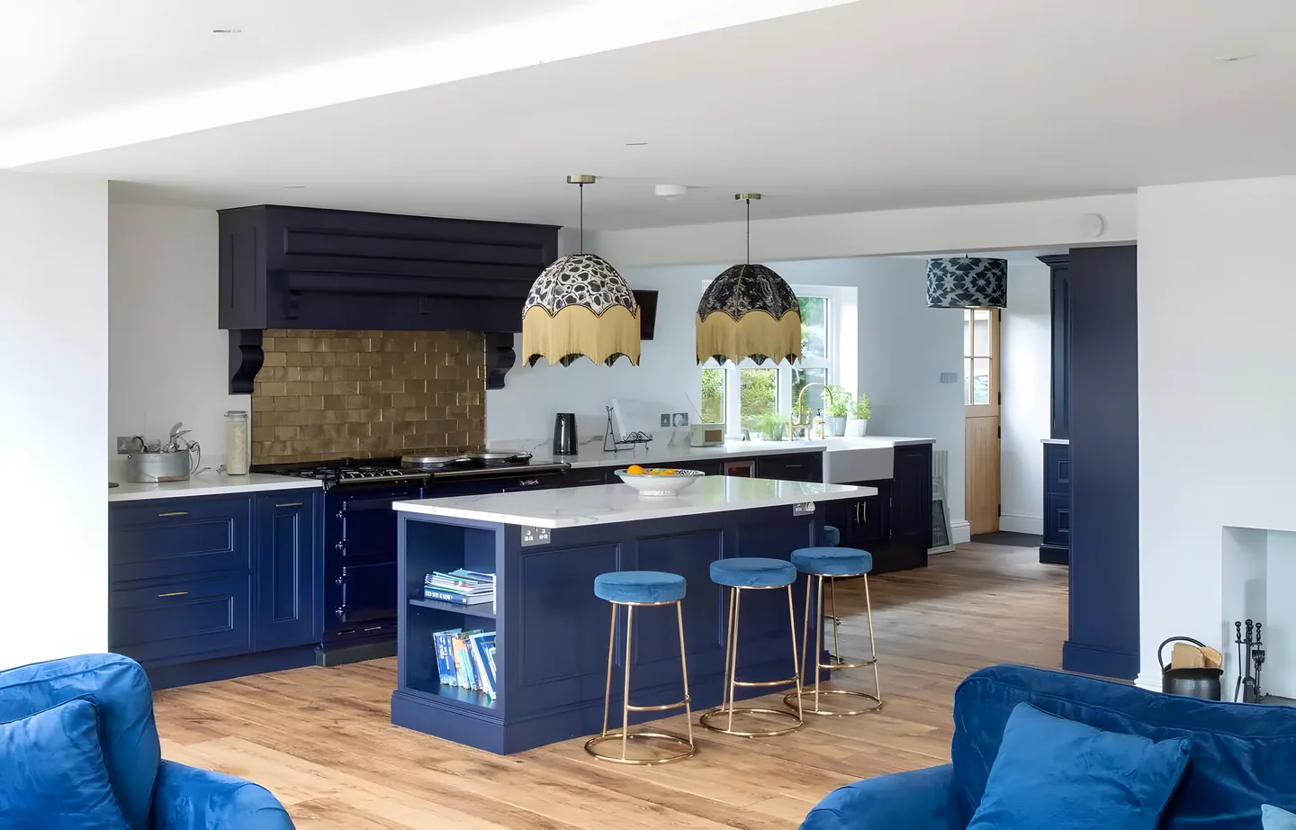 A navy painted island with blue velvet stools and a brick-patterned range recess