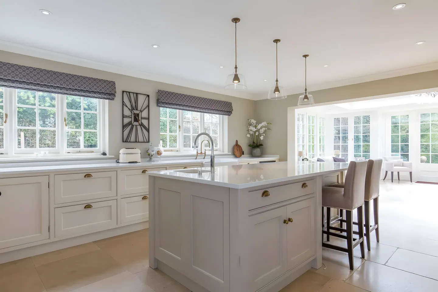 A pale painted island kitchen with pendant lights and a bay of windows