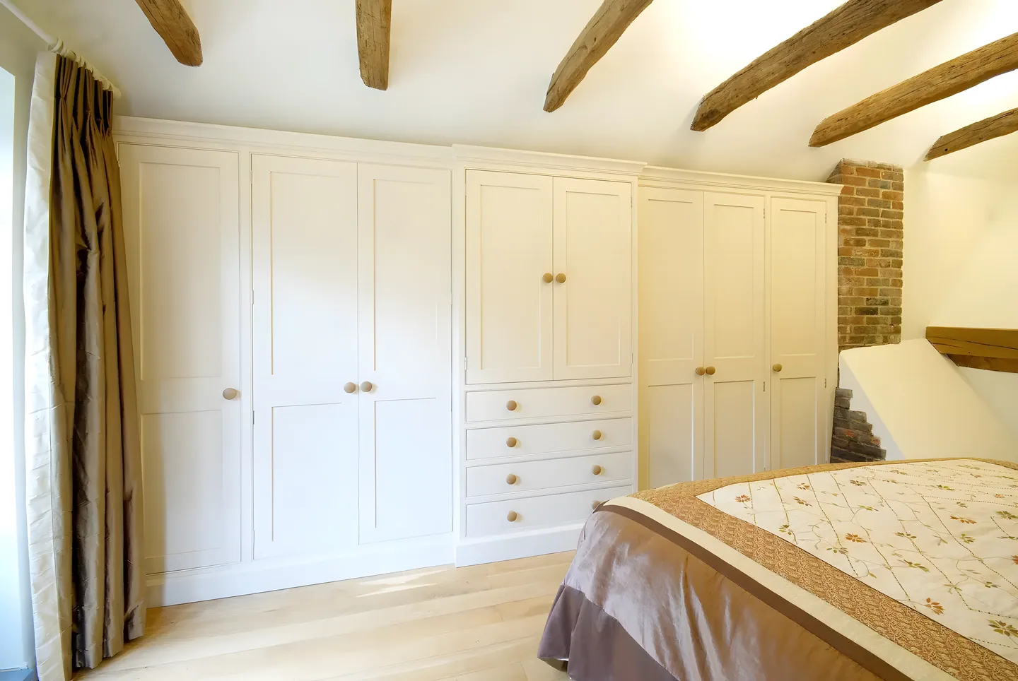 Cream fitted wardrobes with drawers in a beamed bedroom