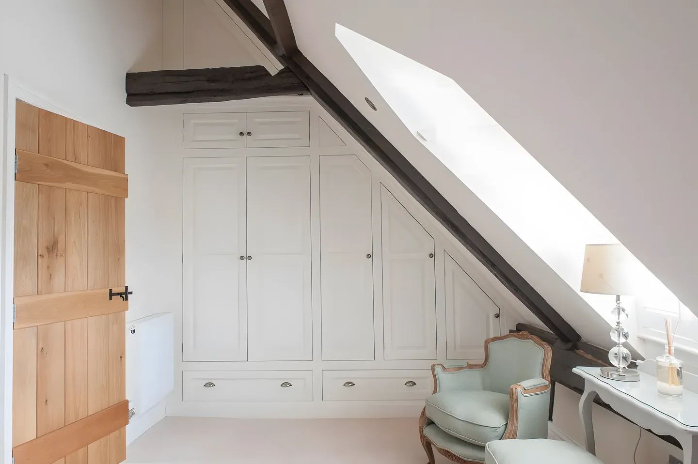 Cream fitted wardrobes tucked under a sloping beamed ceiling